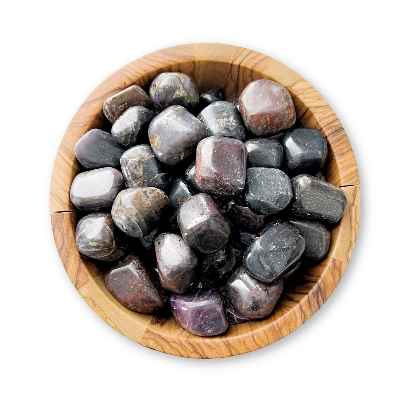 A wooden bowl filled with smooth, polished, dark-hued stones sits against a white background. Among the shades of black, gray, and purple stones are Ruby Corundum Tumbled Stones that assist in emotional healing. Some surfaces have a slight shine, adding to their calming allure.