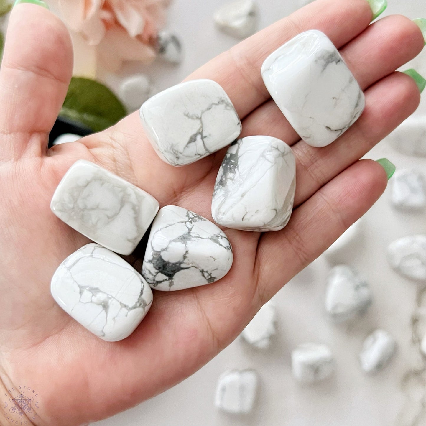 A wooden bowl filled with polished white and gray marble stones, including Howlite Tumbled Stones, on a white background. The Howlite Tumbled Stones vary in size and shape, featuring natural veining patterns of gray on white that promote emotional healing and support the root chakra.