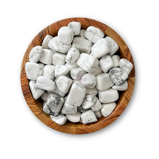 A wooden bowl filled with polished white and gray marble stones, including Howlite Tumbled Stones, on a white background. The Howlite Tumbled Stones vary in size and shape, featuring natural veining patterns of gray on white that promote emotional healing and support the root chakra.