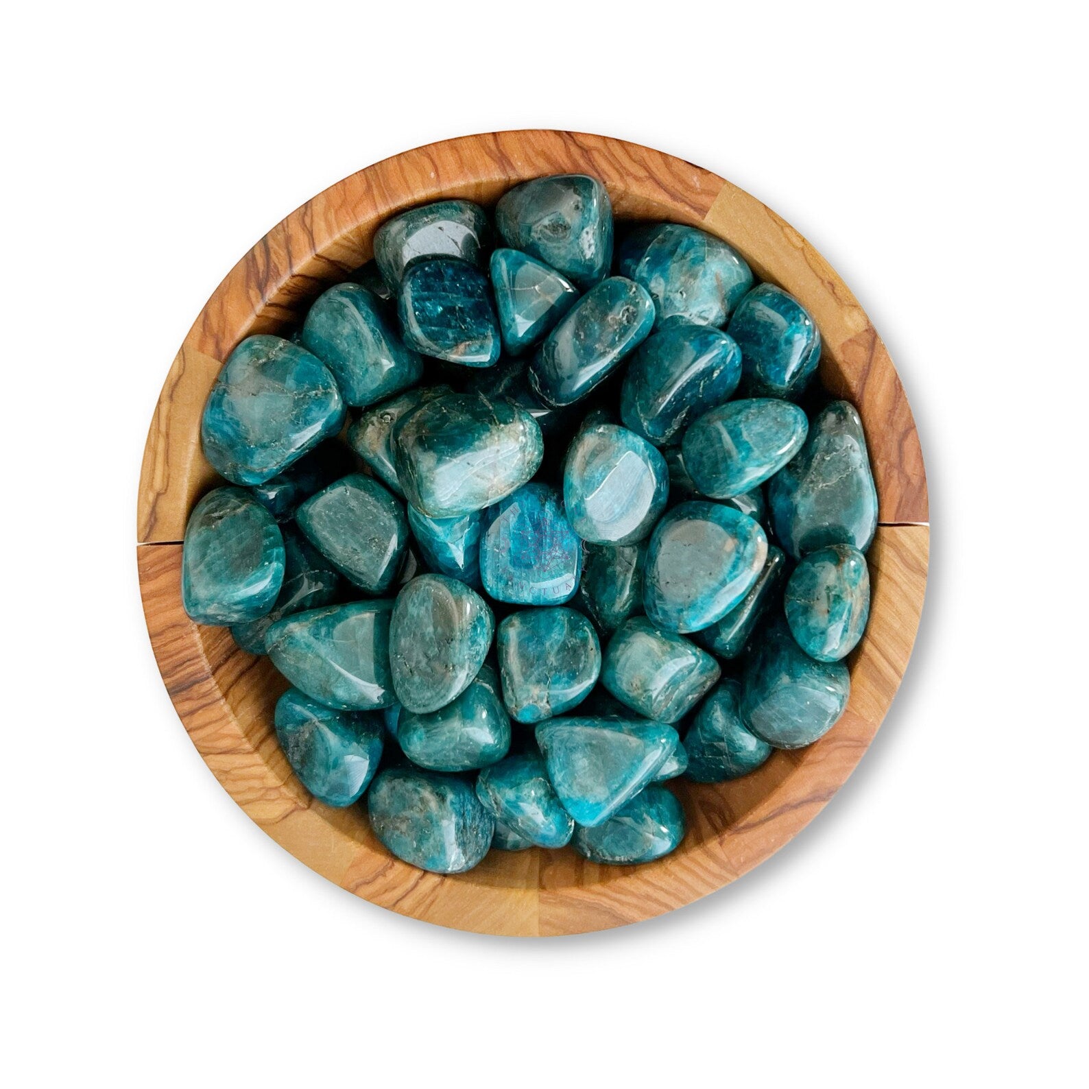 A wooden bowl filled with polished, Blue Apatite Tumbled Stones, known for enhancing psychic gifts and aiding in manifestation, arranged neatly against a white background. The stones have a smooth, shiny surface and vary slightly in shape and size.