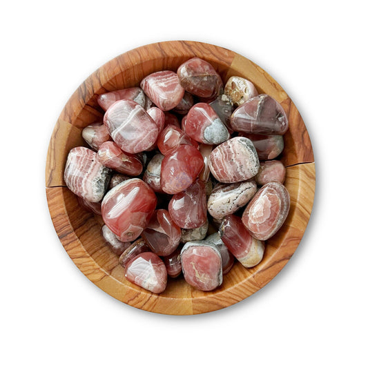 A wooden bowl filled with Grade EX Rhodochrosite Tumbled Stones, known for their emotional healing properties. The stones are smooth with swirling patterns in various shades of red, pink, and white. Perfect for balancing the Heart Chakra, the bowl sits on a plain white background.