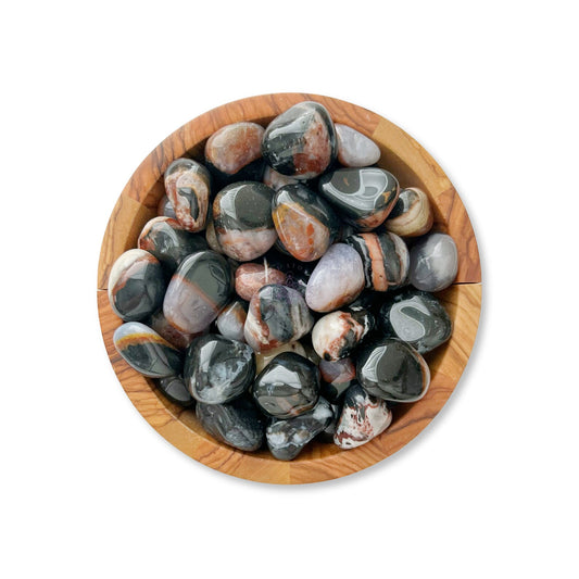 A wooden bowl filled with polished, multi-colored stones in various shades of black, grey, white, and rusty brown. Among them are smooth Sardonyx Tumbled Stones known for bringing happiness and protection. The glossy surfaces display a mix of patterns, arranged neatly within the round bowl.