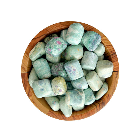 A wooden bowl filled with Ruby Fuchsite Tumbled Stones, viewed from above. The stones have a smooth texture and display a mix of muted green shades with patches of purple dispersed throughout, reminiscent of Ruby in Fuchsite.