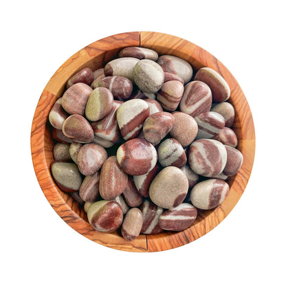 A wooden bowl filled with smooth, polished Shiva Lingam Tumbled Stones of various sizes and shapes. The stones have a mix of earthy colors, including shades of maroon, beige, and light green, creating a visually appealing natural pattern that promotes chakra awakening.