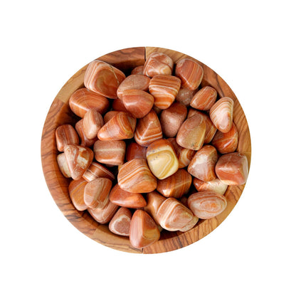 A wooden bowl filled with polished, smooth Red Malachite Tumbled Stones in various shades of orange and brown, showcasing natural striations and patterns, evokes a sense of the Root Chakra's grounding energy. The stones, similar in size with a shiny, glossy finish, rest elegantly on a white background.