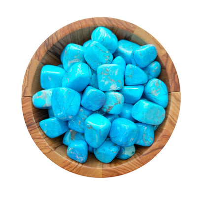 A wooden bowl filled with polished, vibrant Blue Howlite Tumbled Stones. The tumbled crystals have a glossy finish and a mix of bright blue hues with natural, intricate veining patterns. The bowl is set against a plain white background.