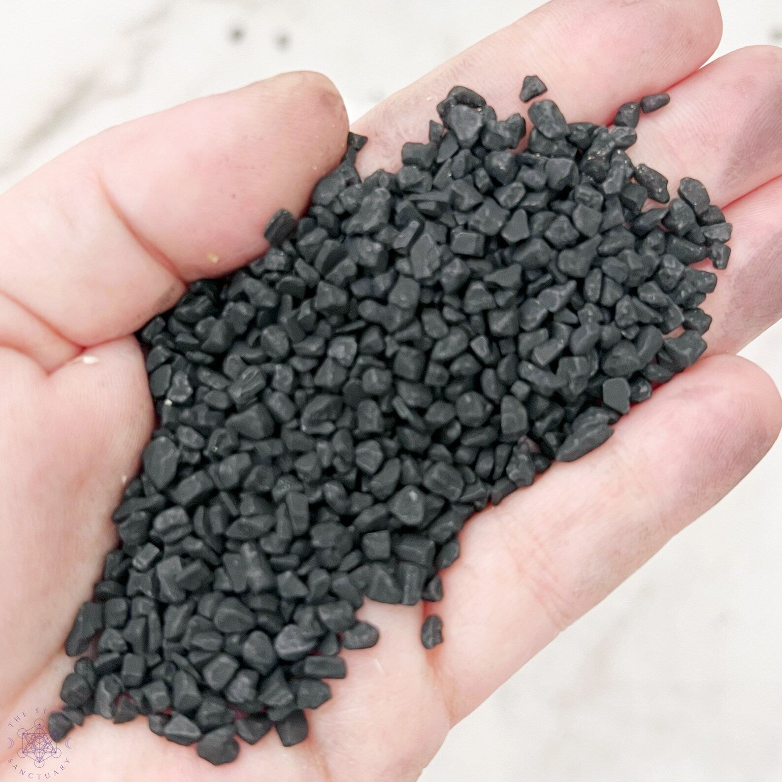 A small sealed package labeled "Black Lava Sea Salt" is placed in front of a glass bowl filled with black salt and a white mortar and pestle. The background features white tiled walls, hinting at the enchanting allure of using Black Salt for Spells with its touch of activated charcoal.