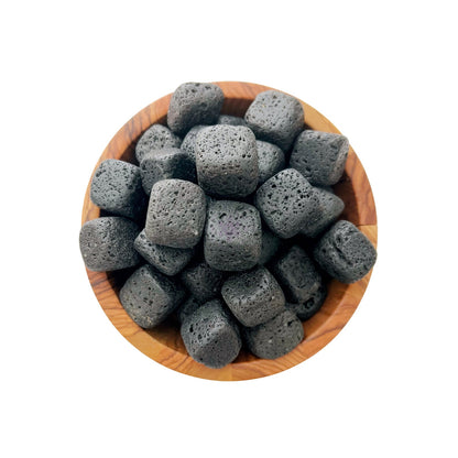 A wooden bowl filled with dark grey, porous, cube-shaped objects. The cubes have an uneven, pitted texture, resembling Lava Rock Tumbled Stones. The white background highlights the contents of the bowl, evoking a sense of a spiritual journey grounded in nature.