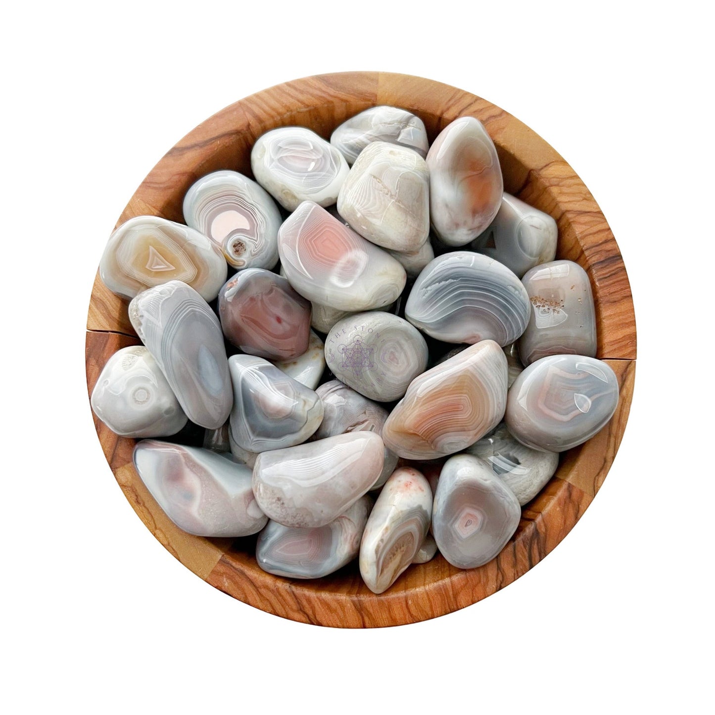 A wooden bowl filled with Pink Botswana Agate Tumbled Stones displaying various shades of gray, white, and subtle hints of pink and peach. The stones have smooth, rounded surfaces and some exhibit banded patterns and concentric circles, perfect for balancing the Heart Chakra.