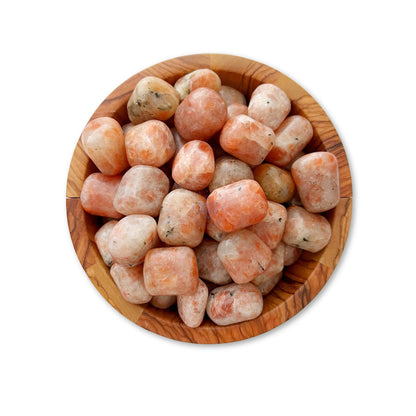 A wooden bowl filled with polished, round Sunstone Tumbled Stones. The stones vary in shades of peach with some white and grey inclusions. The bowl's grain adds a natural contrast to the smooth, semi-translucent stones that are said to bring luck and good fortune.