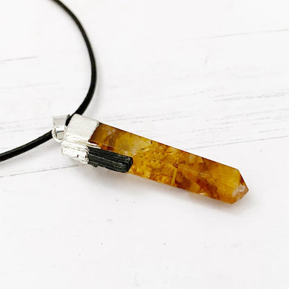 A 1" Golden Healer Quartz Point Pendant featuring a polished, faceted Golden Healer Quartz with warm yellow and brown tones. The crystal is capped with a silver plated cap and hangs from a black cord. The background is plain white.