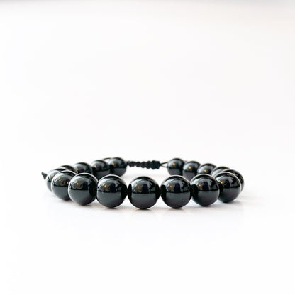 The 10mm Black Obsidian Beaded Bracelet is a minimalist piece characterized by shiny black beads that are evenly spaced and threaded on a black cord. Known for its protective qualities, this adjustable bracelet is presented against a plain white background to highlight its simplicity and elegance.