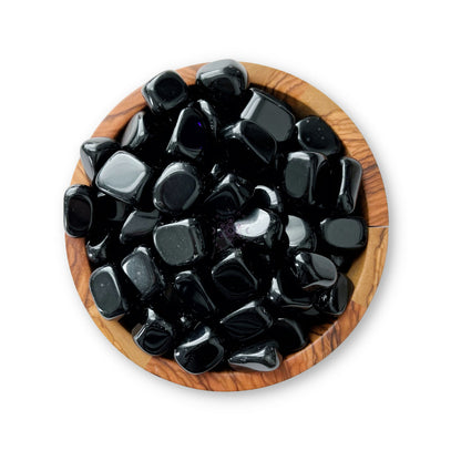 A wooden bowl filled with smooth, polished Black Obsidian Tumbled Stones against a white background. The Black Obsidian Tumbled Stones are shiny and uniformly rounded, creating a visually appealing contrast with the natural wood grain of the bowl.