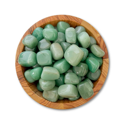 A wooden bowl filled with smooth, polished Green Aventurine Tumbled Stones, known as the "Stone of Opportunity." The stones are uniform in size with a glossy finish, enhancing their various shades of green. Often associated with the Heart Chakra, the bowl is placed against a plain white background.