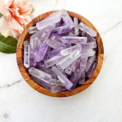 A 1-2" Polished Amethyst Point arranged upright on a smooth surface. The crystals, perfect for energy generators or crystal grids, vary in size and shape, with multiple facets catching the light and revealing the natural inclusions within the stones. A blurred background adds depth.