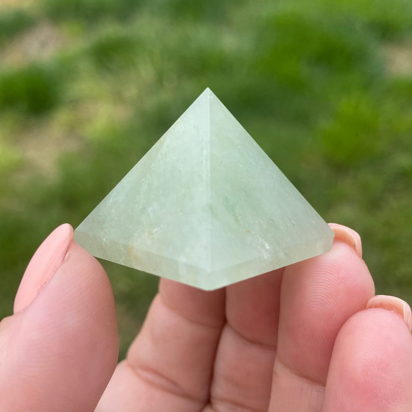 Three 1" Mini Green Aventurine Pyramids are arranged on a white wooden surface with a bundle of sage in the background. Perfect for meditation, the scene is set against white tiled walls.