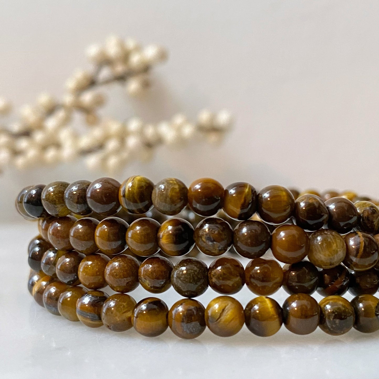 A 4mm Tigers Eye Beaded Bracelet, made of natural stone with spherical beads in golden yellow and brown hues, lies coiled on a shiny black surface. The reflective surface enhances the glossy appearance of the Reiki-infused bracelet.