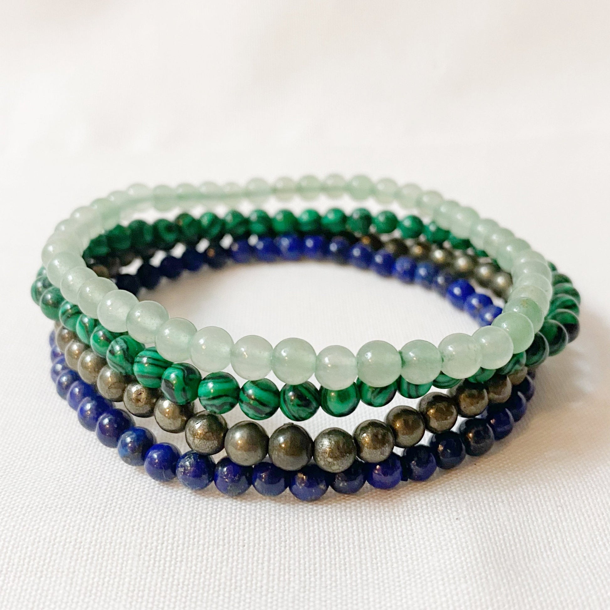 Image of a Taurus Bracelet Set featuring four Reiki Infused Energy Bracelets in shades of green and blue, including Green Aventurine, Malachite, Pyrite, and Lapis Lazuli. Text highlights Taurus traits and date range (April 20 - May 20). The background is white.