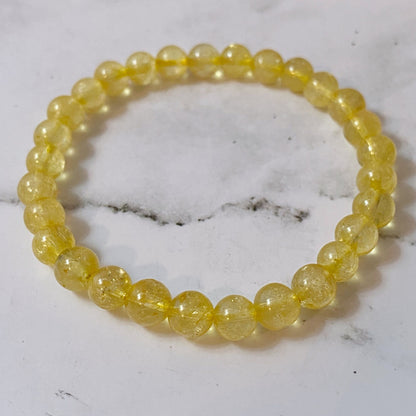 A 6mm Citrine Beaded Bracelet is displayed against a black background. The polished beads have a translucent quality and reflect light, giving the bracelet a radiant appearance. Known for its Usui Reiki energy, this manifestation stone adds a touch of magic to your wrist.