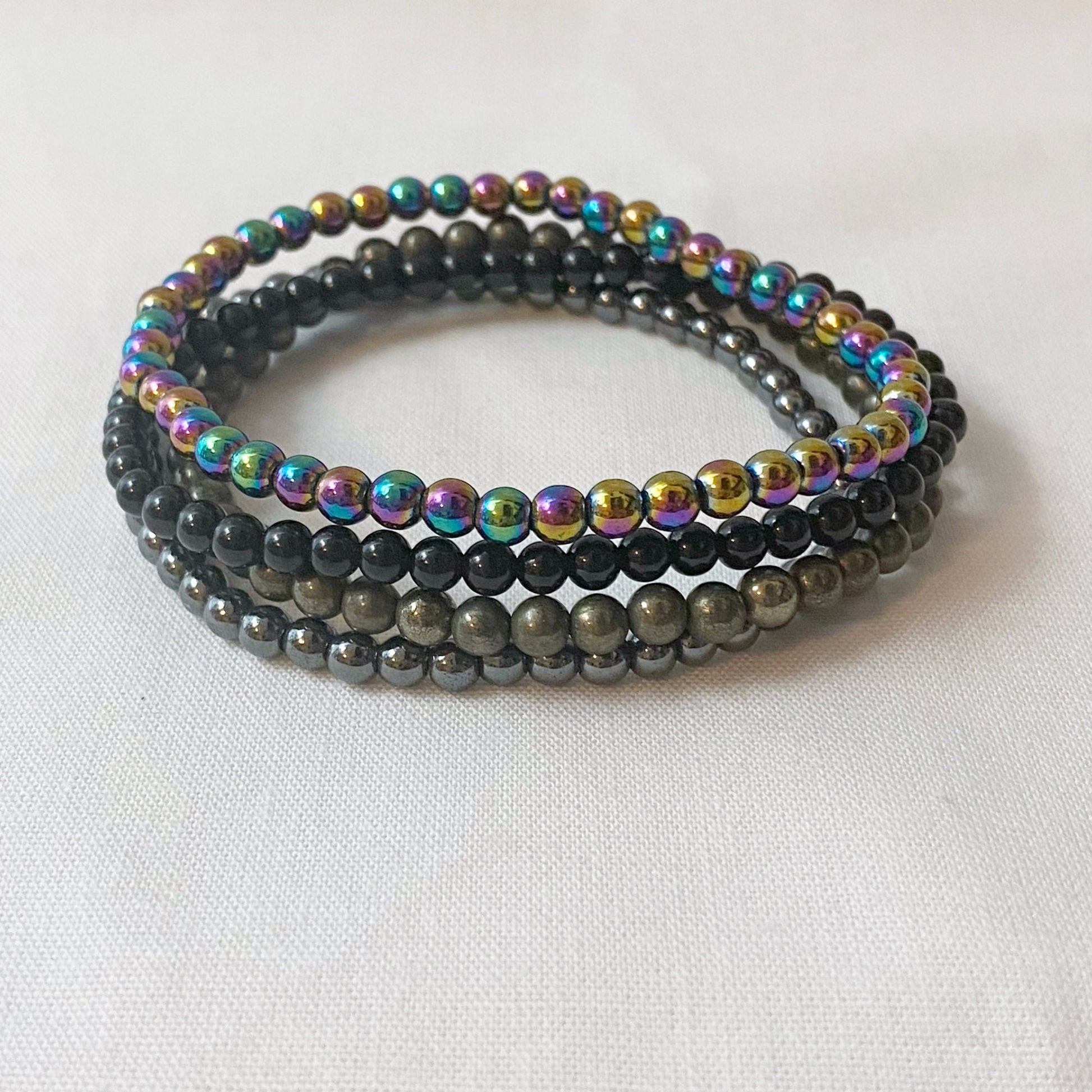 Image showing a set of Energy Protection Bracelet Set made from various beads. The text highlights the bracelet’s materials: Rainbow Hematite, Black Tourmaline, Pyrite, and Hematite. It states the bracelets provide protection from negativity and EMFs, and support physical, mental, and spiritual health.