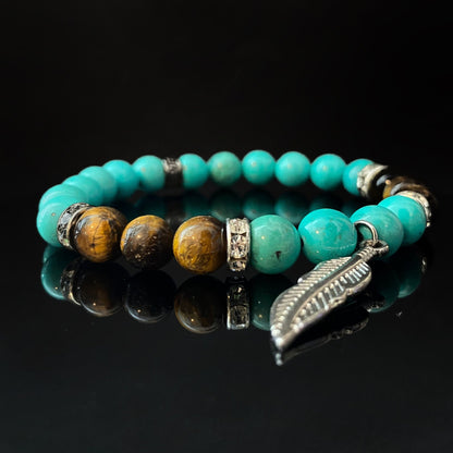 An 8mm Turquoise & Tiger Eye Beaded Bracelet with Feather Charm featuring gemstone beads with brown tiger eye beads interspersed. Several beads have surrounding silver embellishments, and a silver feather charm is attached, all displayed against a black background.