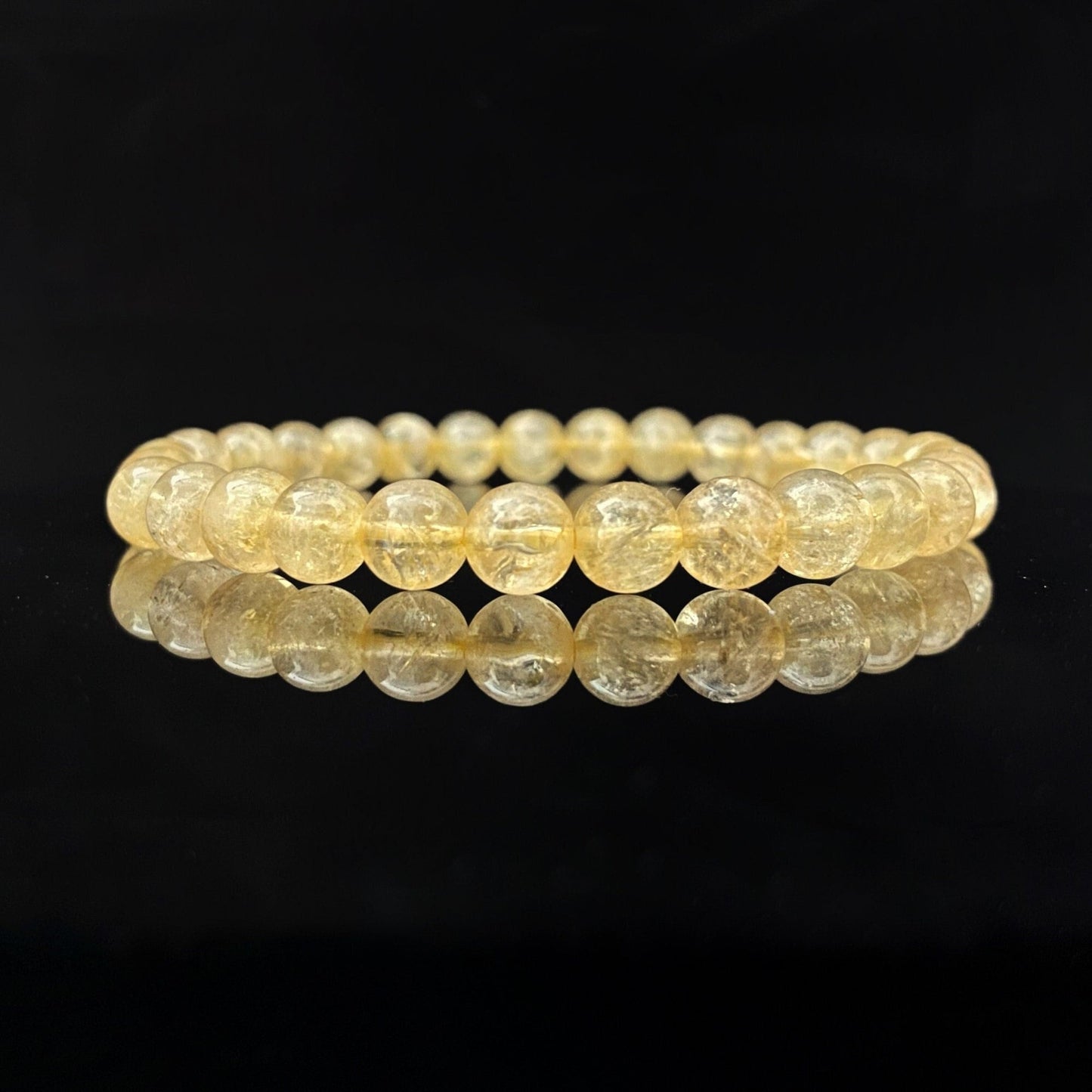 A 6mm Citrine Beaded Bracelet is displayed against a black background. The polished beads have a translucent quality and reflect light, giving the bracelet a radiant appearance. Known for its Usui Reiki energy, this manifestation stone adds a touch of magic to your wrist.