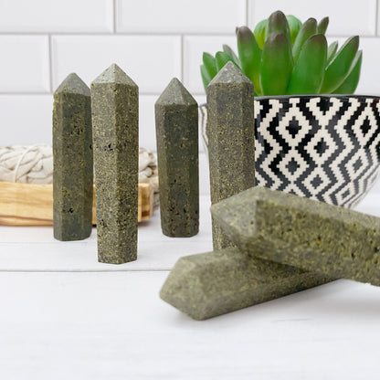 Image showing a set of 2-3" Epidote Point, standing upright on a white wooden surface. In the background, there is a succulent plant in a black-and-white patterned pot, and a light-colored woven mat is partially visible.