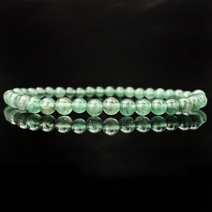 A delicate 4mm Green Aventurine Beaded Bracelet made of polished green beads is centered against a black background. The uniform beads highlight its stretchable design, and the bracelet's reflection shimmers below it on the reflective surface.