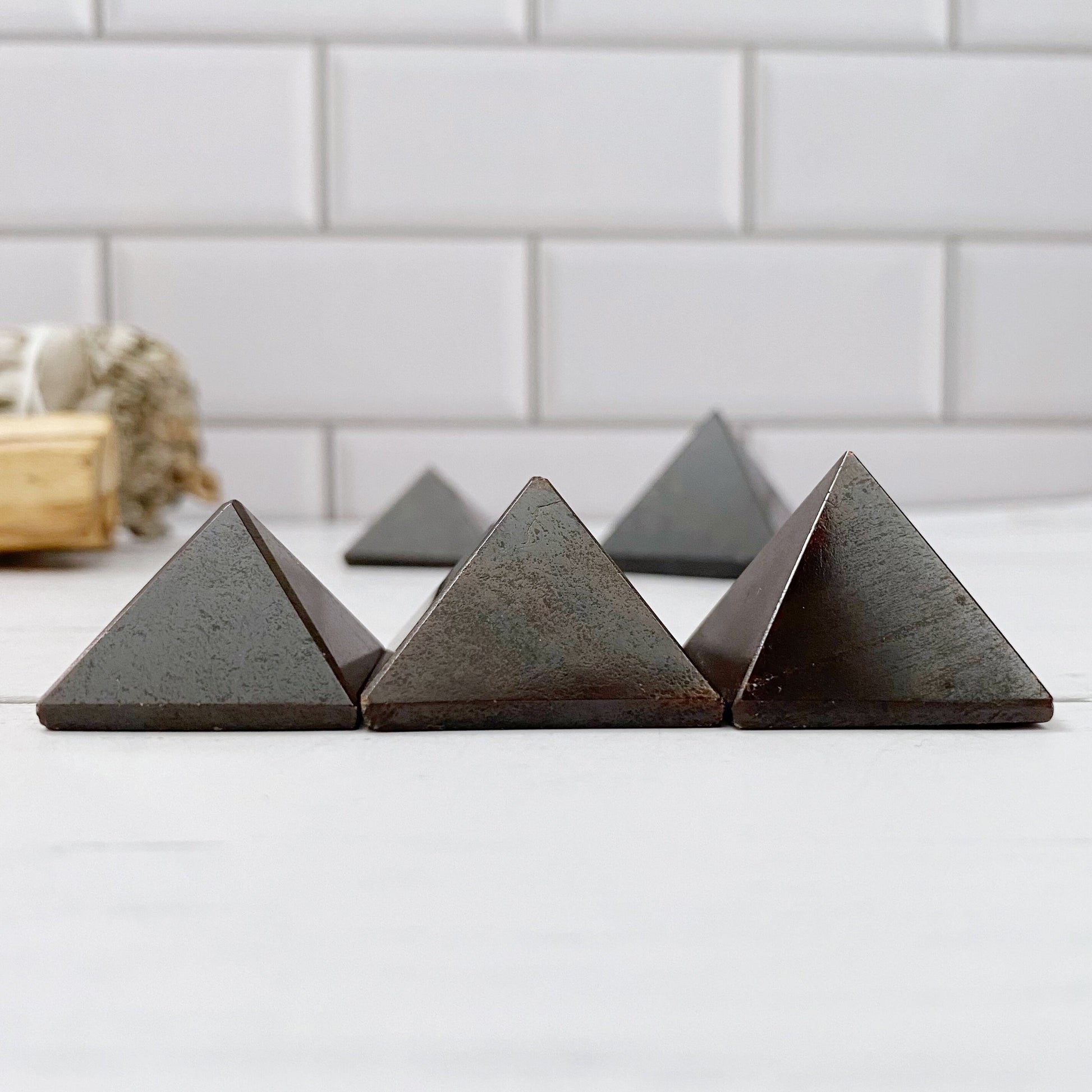 Three 1" Mini Garnet Pyramids, likely made of stone or crystal, are placed in front of a bundle of sage tied with twine. The scene is set against a white tiled background. The objects and sage are on a light-colored surface, creating a minimalist aesthetic perfect for chakra cleansing and emotional balance.