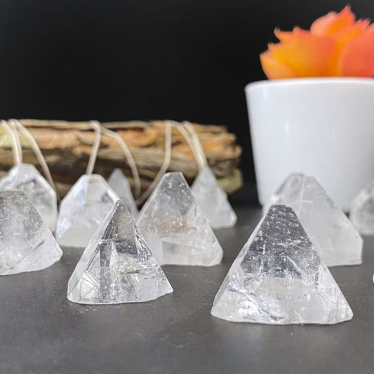 Several small, high vibrational Raw Apophyllite Crystal Points are arranged on a dark surface. In the background, there is a bundle of sticks tied together and a white pot containing an orange succulent. The scene, featuring these powerful crystals, is set against a plain dark backdrop.