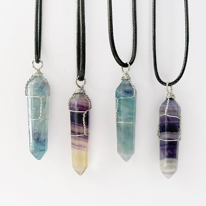 Four 1.5" Double Terminated Rainbow Fluorite Wire Wrapped Pendants hang from black cords against a white background. The crystals, wire-wrapped in silver, display gradient hues of blue, purple, green, and clear, showcasing their natural variations and polished finish.