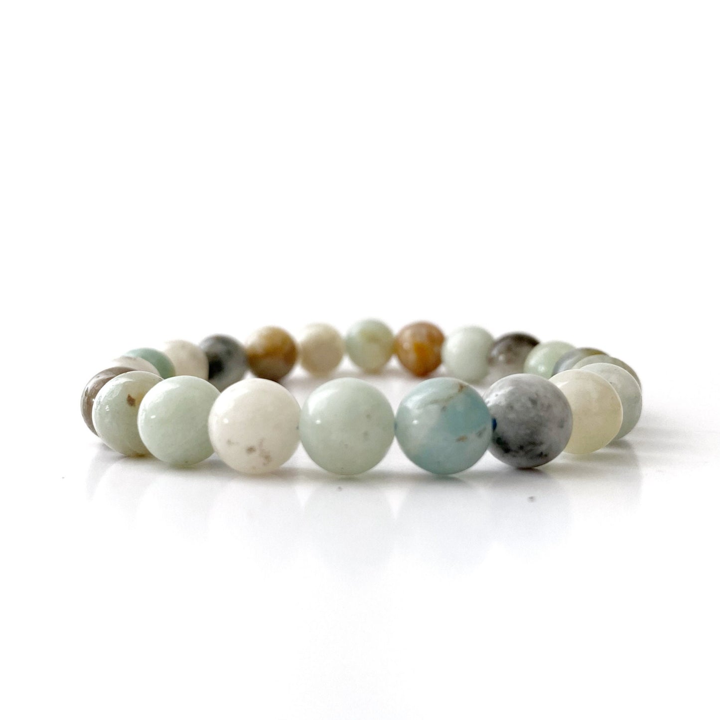 A beaded bracelet made of round, polished beads in various soothing hues, including shades of white, light blue, tan, grey, and mint green. This 8mm Amazonite Beaded Bracelet is arranged in a circle and set against a clean, white background.