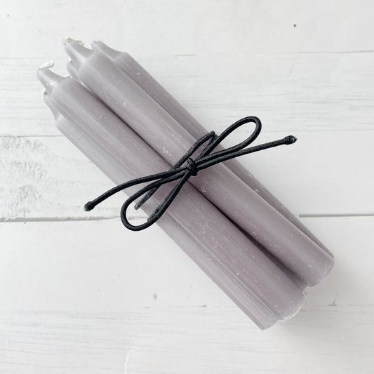 Four 5" Gray Chime Candles are bundled together with a black string, placed on a white wooden surface. The chime candles have white wicks and a slightly textured finish, perfect for spellwork or ceremonial use.