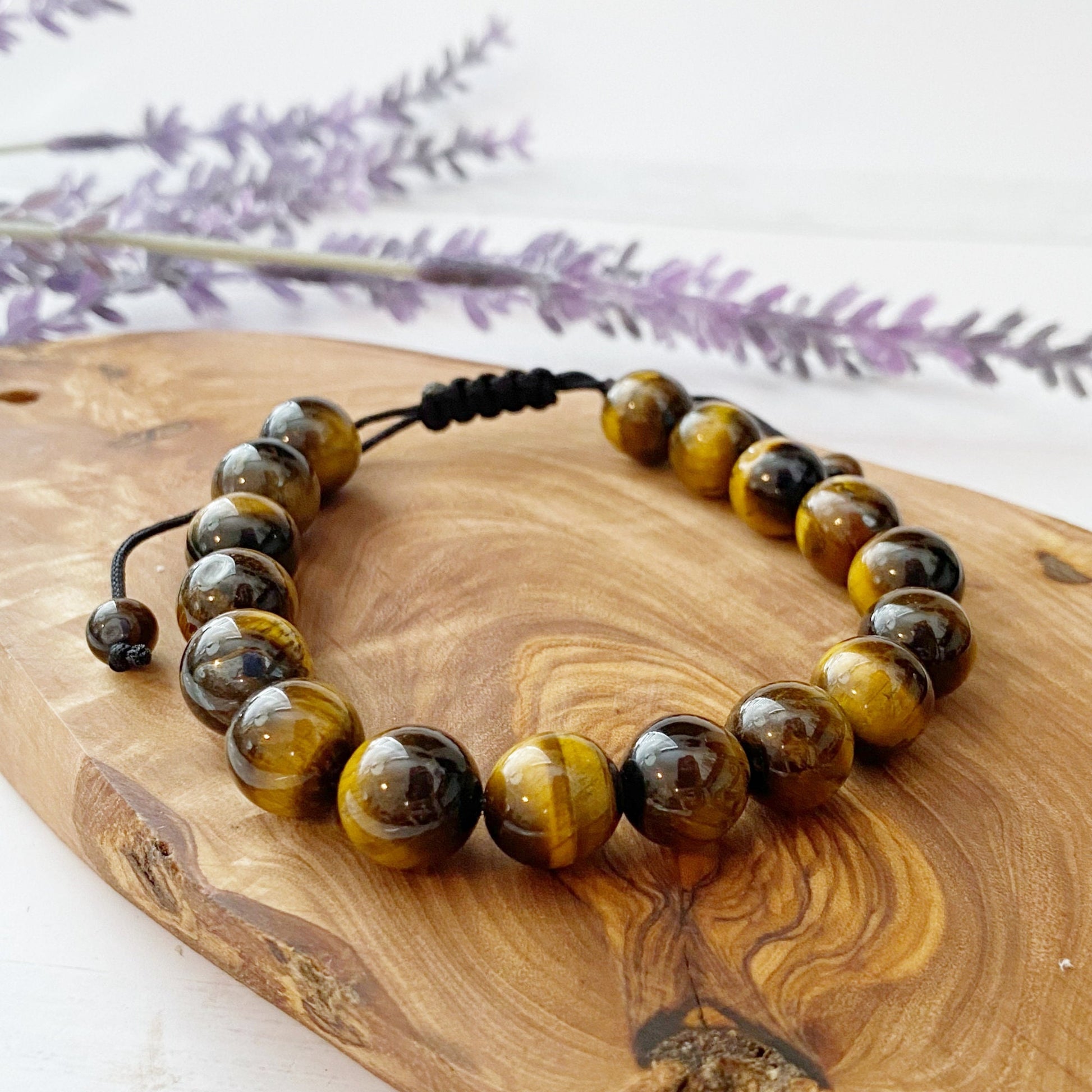 A polished 10mm Tiger Eye Beaded Bracelet with smooth, round beads strung together on a black cord. The beads showcase a blend of golden brown, yellow, and dark brown hues with a reflective sheen, lying on a white background. This beaded bracelet harmonizes the natural beauty of the stone with serene Usui Reiki energy.
