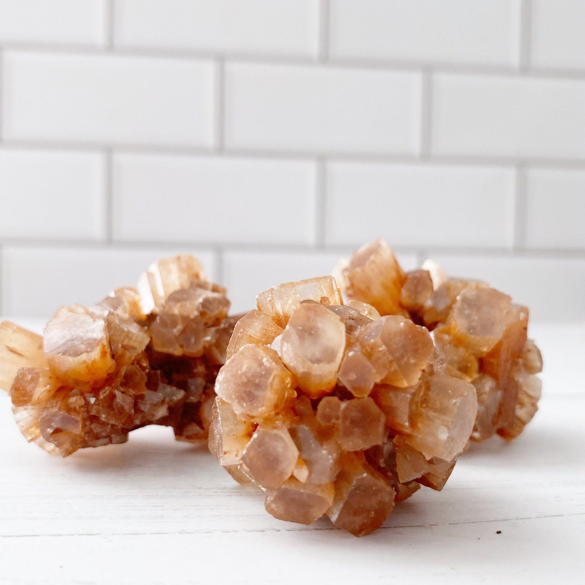 Two clusters of Raw Aragonite Cluster rest on a white surface with white subway tile in the background. The hexagonal shapes appear translucent, showcasing their intricate geometric formations, perfect for chakra balancing and grounding stone practices.