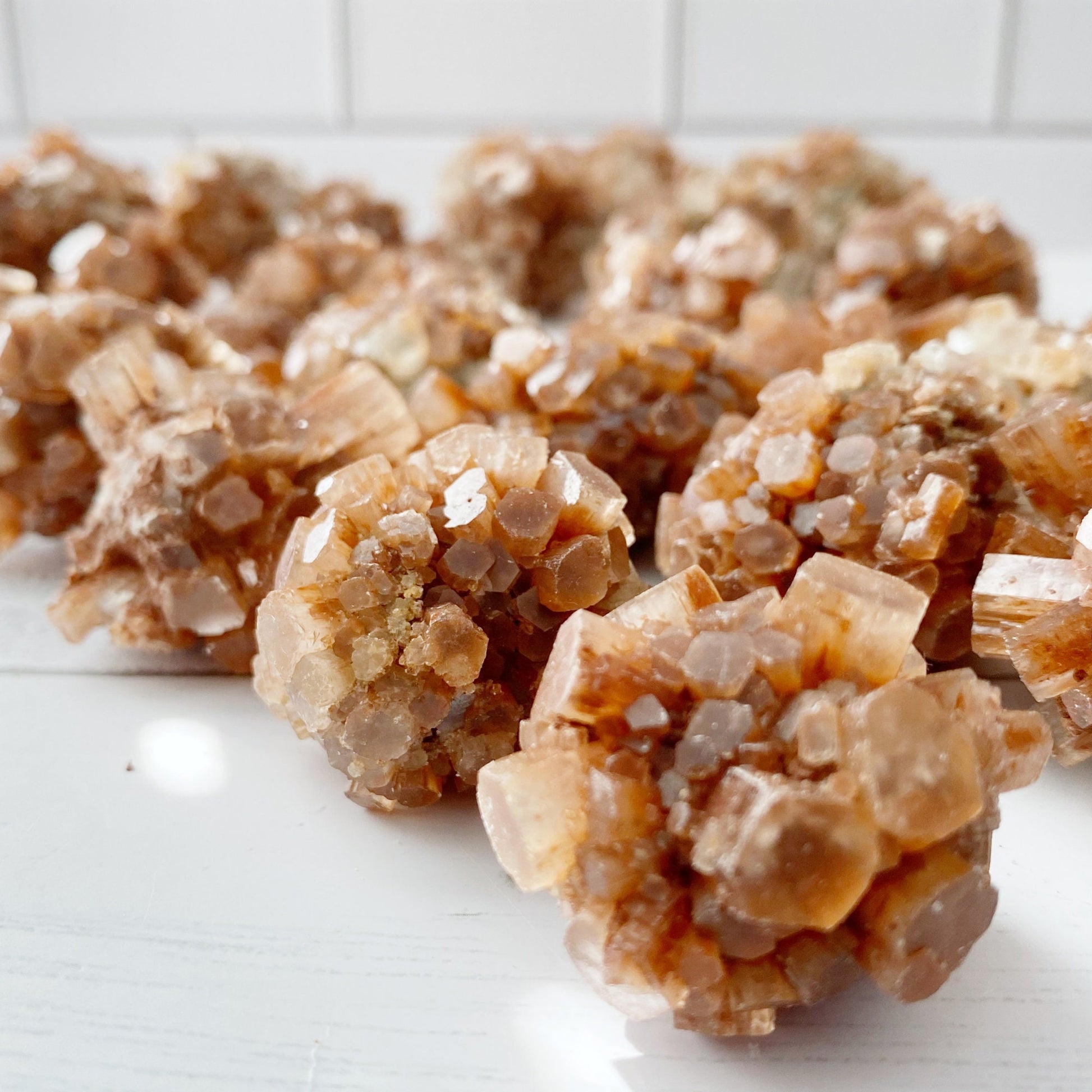 Two clusters of Raw Aragonite Cluster rest on a white surface with white subway tile in the background. The hexagonal shapes appear translucent, showcasing their intricate geometric formations, perfect for chakra balancing and grounding stone practices.