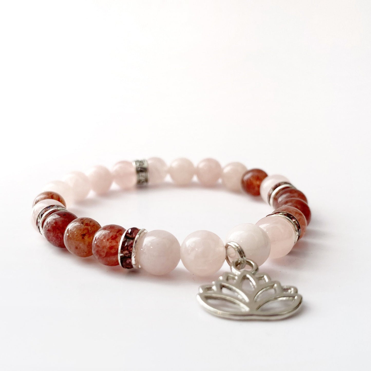 8mm Rose & Strawberry Quartz Beaded Bracelet w/Lotus Charm featuring alternating light pink and brownish-red beads with silver spacers. Accented with a lotus flower charm in silver, the design showcases Strawberry Quartz and Rose Quartz beads, displayed elegantly on a white background.