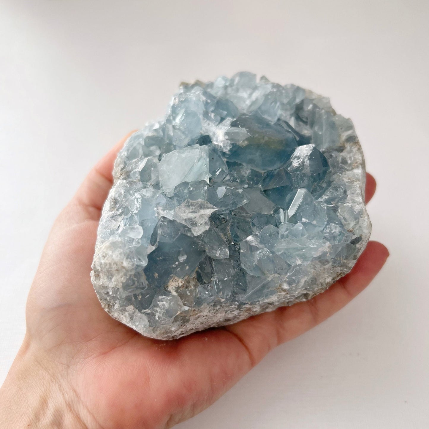 A 1-2 lbs Large Celestite Cluster sits on a patch of vibrant green grass. The crystal features multiple, sharp-edged facets that catch the light, creating a sparkling effect reminiscent of the angelic realm.