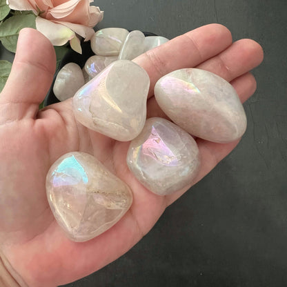 A wooden bowl filled with polished moonstones displaying a translucent, milky appearance with hints of ethereal, iridescent sheen. The stones vary slightly in size and shape but share the glowing quality of moonstone. This collection enhances heart healing and positive energy, much like Angel Aura Rose Quartz Tumbled Stones.