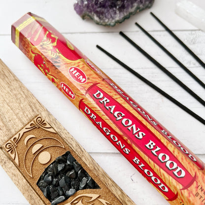 Image of a box and a tube of Dragon's Blood Incense Sticks, perfect for meditation yoga. The packaging features a red design with yellow dragons and a textured background. The rectangular box and cylindrical tube clearly showcase the product name, ideal for enhancing your witchcraft Wicca rituals.