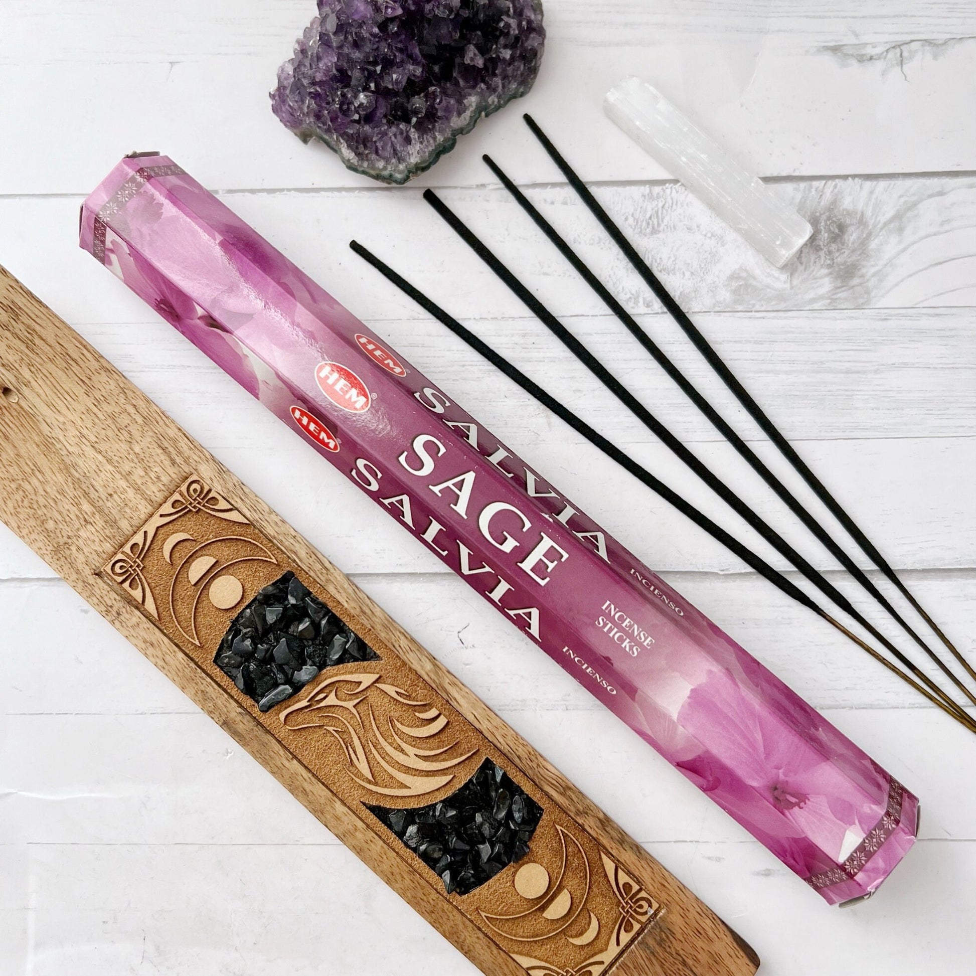 Two packs of Sage Incense Sticks are shown. The boxes, adorned with purple and white floral patterns, are designed to cleanse spaces. One box stands upright while the other lies horizontally. Both feature the HEM brand logo and the word "SAGE" prominently on the front, showcasing this traditional incense.