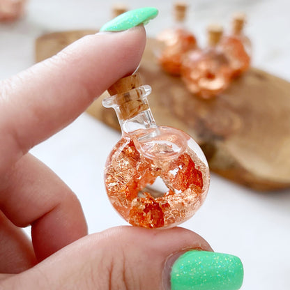 Six Copper Flakes Bottles with cork stoppers are filled with shimmering copper flakes, ideal for chakra healing and other metaphysical practices. The bottles are arranged on a wooden surface with a blurred background, highlighting the intricate texture and vibrant color of the copper inside the clear jars.