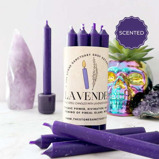 A group of 5" Lavender Scented Purple Chime Candles are displayed on a white surface. The background includes decorative items like an amethyst point, a holographic skull, and a small cluster of crystals. Ideal for meditation rituals with the calming Lavender essential oil scent, indicated by the "Scented" sticker at the top right corner.