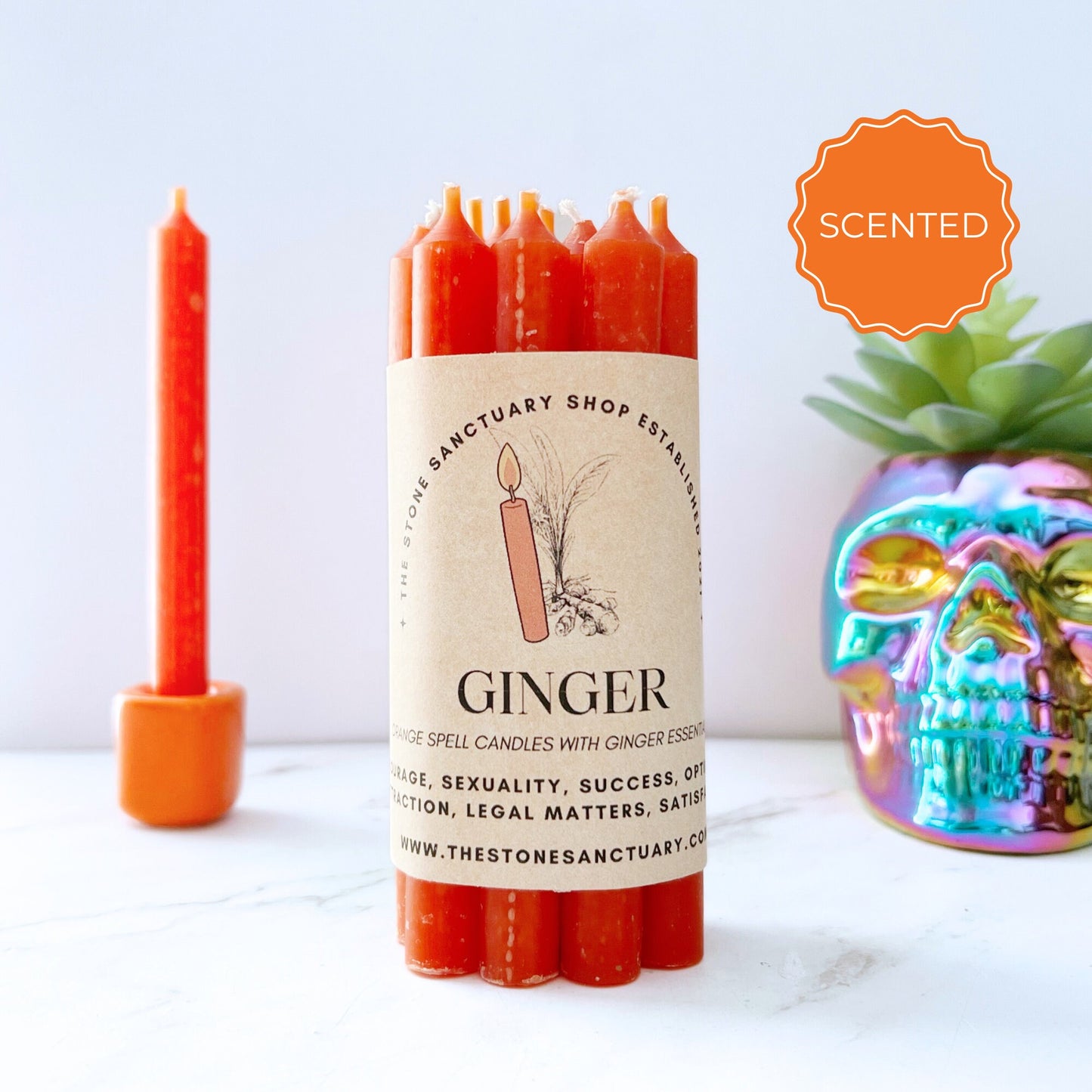 A bundle of reddish-orange candles labeled "5" Ginger Scented Orange Chime Candles," designed for health and success intentions, showcased beside a shiny, multi-colored skull decoration. One 5" Ginger Scented Orange Chime Candle stands upright in the background. Infused with ginger essential oil to spark creativity and confidence, a "Scented" badge is displayed prominently.