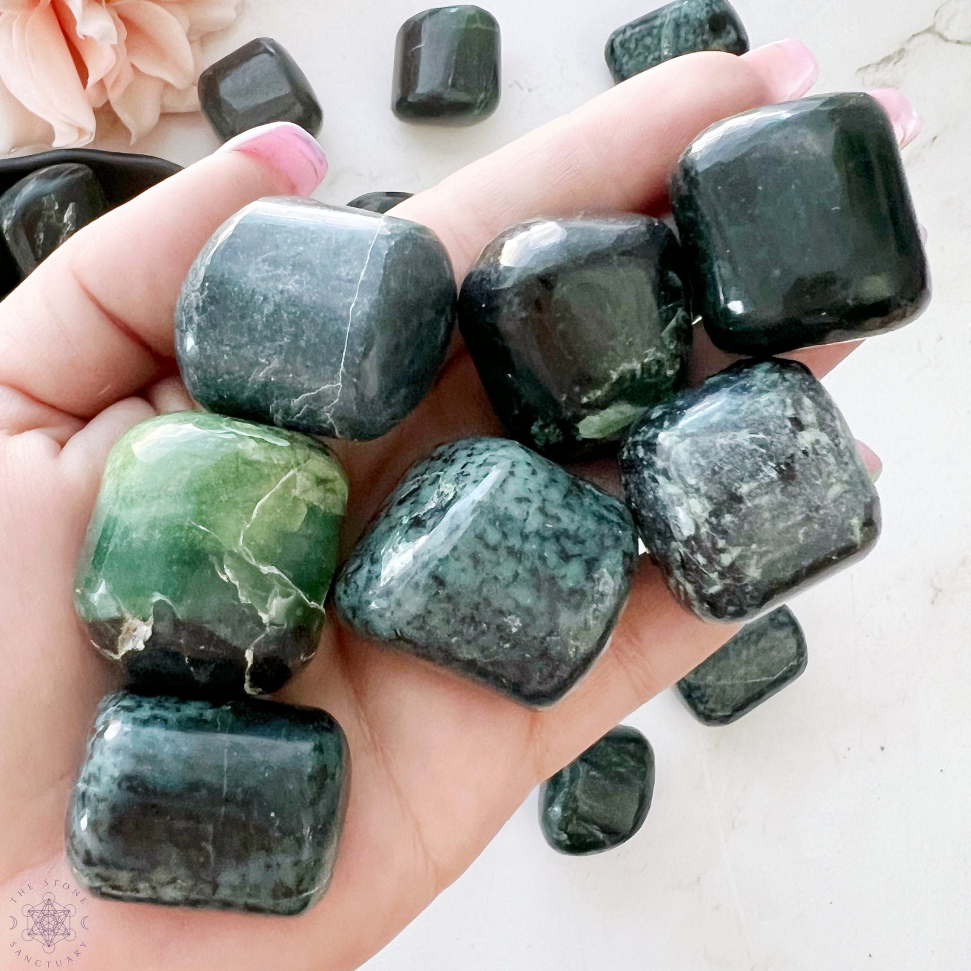 A wooden bowl filled with smooth, polished Green Kyanite Tumbled Stones, perfect for chakra alignment. The stones have a glossy finish and are irregular in shape, fitting snugly within the bowl. The background is plain white.