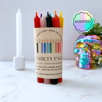 A Variety Pack Scented Chime Candles is displayed on a marble surface. The pack contains six different colored candles, each aligned with chakra balancing, and showcases a label with multiple candle illustrations. Nearby, a tall white candle is visible, along with a colorful, reflective skull decoration.