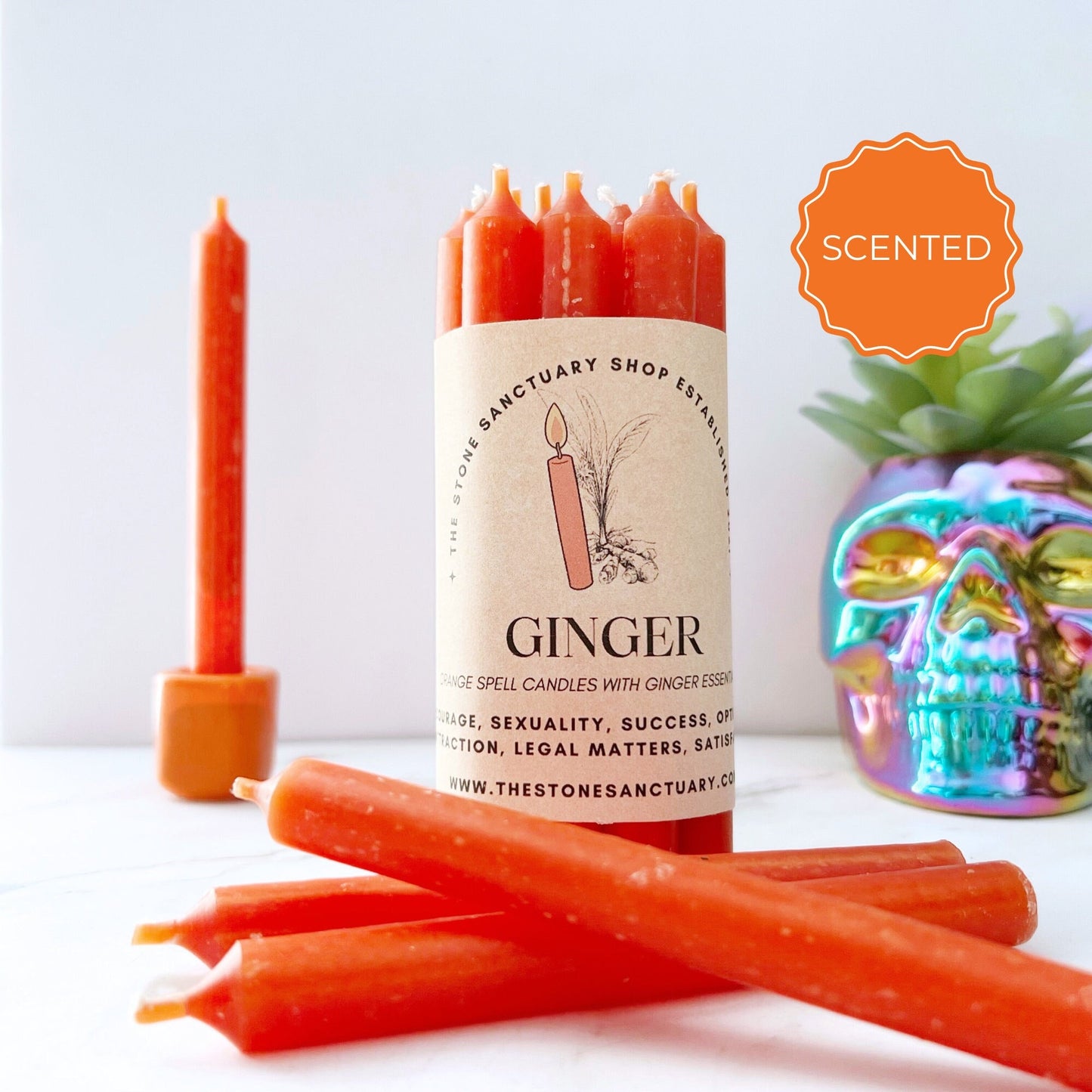 A bundle of reddish-orange candles labeled "5" Ginger Scented Orange Chime Candles," designed for health and success intentions, showcased beside a shiny, multi-colored skull decoration. One 5" Ginger Scented Orange Chime Candle stands upright in the background. Infused with ginger essential oil to spark creativity and confidence, a "Scented" badge is displayed prominently.