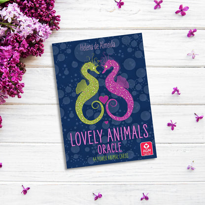 A blue box titled "Lovely Animals Oracle" features two colorful, intricately decorated seahorses facing each other, forming a heart shape with pink hearts between them. The box sits on a white wooden surface surrounded by purple flowers, celebrating the beauty of the animal kingdom.