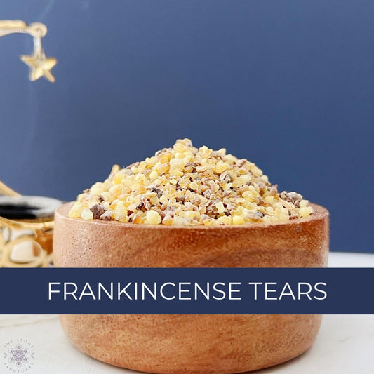 A wooden bowl filled with small, yellowish resin pieces labeled "Frankincense Tears" sits on a white surface against a dark blue background. Revered in spiritual practice, Frankincense Tears is accompanied by a small section of a decorative item with a star visible on the left.